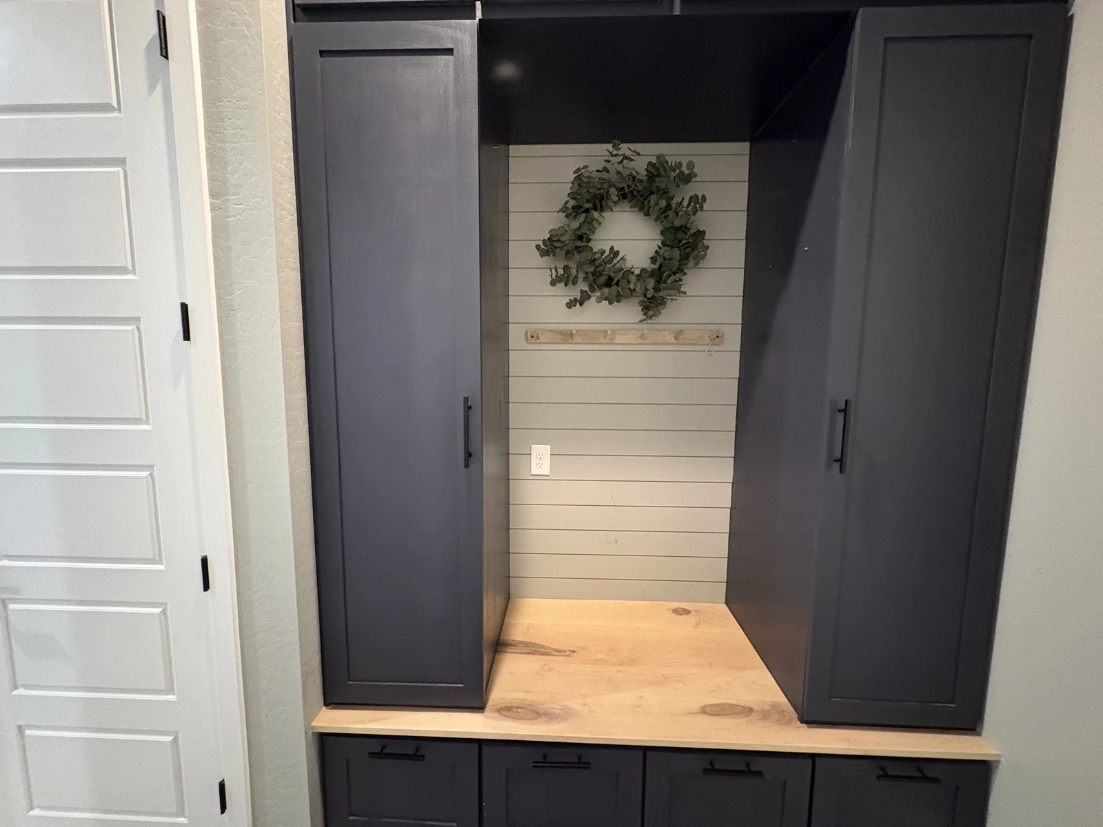 Front view of dark entry storage cabinetry and paneled backdrop
